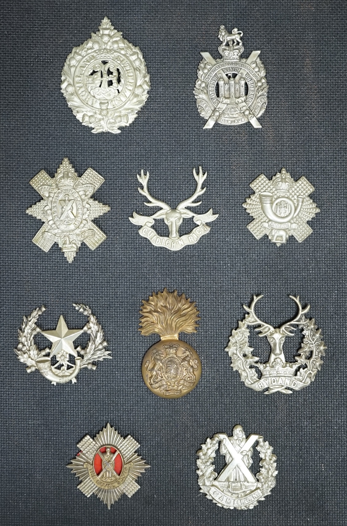 Ten military cap and Glengarry badges mounted on a board including; The King’s Own Scottish Borderers, the Argyle and Sutherland Regiment, the Royal Scots, the Gordon Highlanders, The Queen’s Own Cameron Highlanders, etc